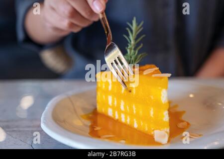 Immagine closeup di una mano che taglia un pezzo di torta d'arancia da mangiare con forchetta in bar Foto Stock