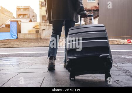 Immagine di primo piano di una donna che cammina mentre viaggia e trascina un bagaglio nero all'aperto Foto Stock