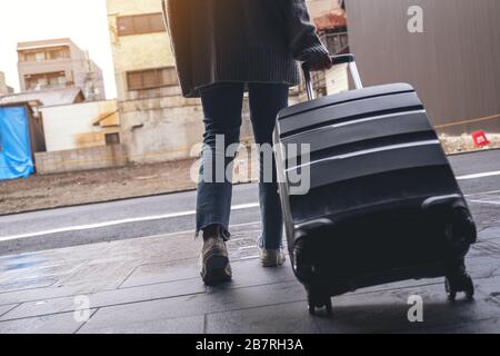 Immagine di primo piano di una donna che cammina mentre viaggia e trascina un bagaglio nero all'aperto Foto Stock