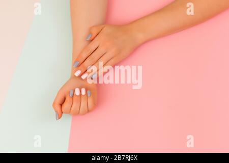 Elegante manicure femminile alla moda. Bella mano di giovane donna con perfetto manicure rosa e grigio su sfondo grigio blu rosa. Stile piatto. Foto Stock