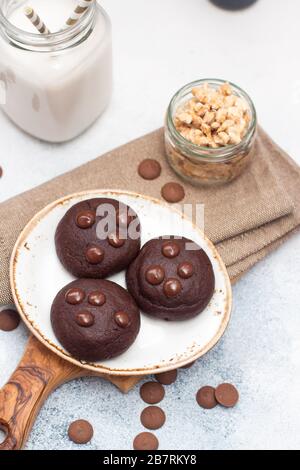 Biscotti al cioccolato con gocce di cioccolato su piastra bianca e bicchiere di latte su sfondo grigio Foto Stock