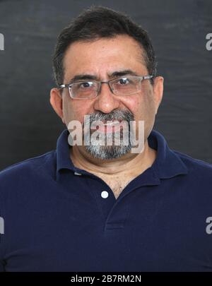 Un uomo indiano sorridente con un portiere in uno studio su uno sfondo scuro. Indossare occhiali e guardare la fotocamera. Foto Stock
