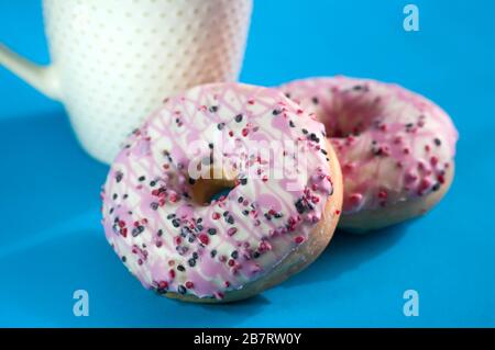Ciambelle smaltate con una tazza di caffè su sfondo blu. Foto Stock