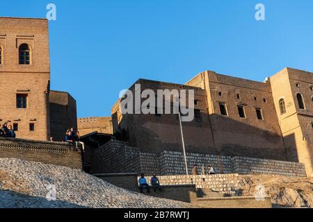 Iraq, Kurdistan iracheno, Arbil, Erbil. Vista della cittadella di Erbil Qalat al tramonto. Gli adolescenti sono seduti ai bordi del parapetto Foto Stock