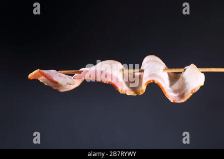 Pancetta su uno spiedino su uno sfondo nero Foto Stock