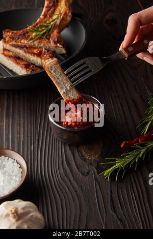 Vista tagliata della donna che mette la fetta di bistecca in salsa di pomodoro da aglio e sale sulla superficie di legno Foto Stock