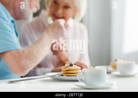 Fuoco selettivo di coppia senior sorridente l'un l'altro da caffè e pancake sul tavolo Foto Stock