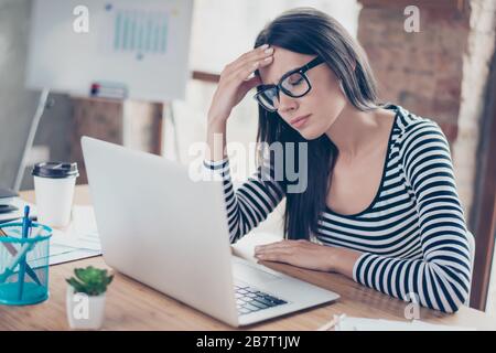 Stanco overwokred giovane donna d'affari in occhiali seduti al tavolo e toccando la fronte Foto Stock