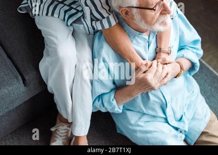 Vista dall'alto di un uomo anziano che tiene le mani della moglie mentre si siede sul pavimento a casa Foto Stock