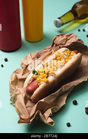 hot dog con mais e bottiglie con birra, senape e ketchup su blu Foto Stock