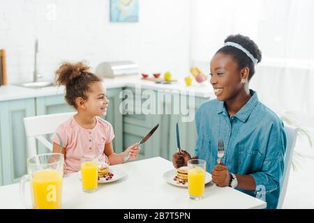 allegra madre e figlia afro-americana che tiene posate vicino gustosi pancake Foto Stock