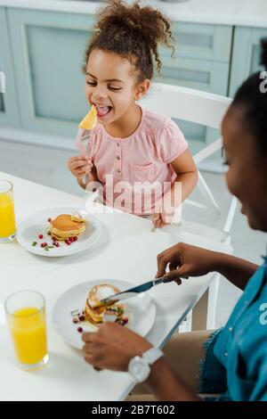 fuoco selettivo di capretto africano felice americano che mangia le frittelle vicino alla madre Foto Stock