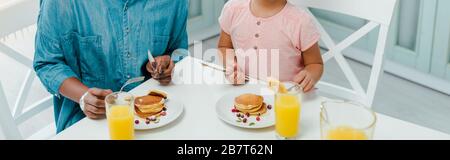 foto panoramica di madre e figlia afro-americana con posate vicino a frittelle Foto Stock