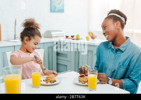 felice madre afro-americana guardando la figlia vicino a gustosi pancake Foto Stock
