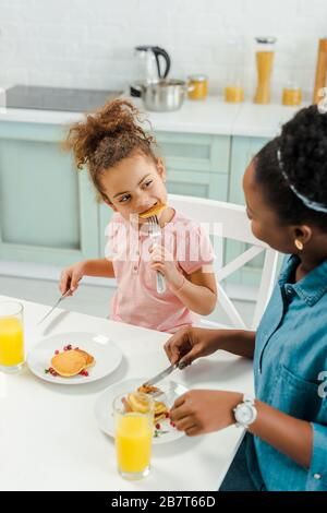 madre africana americana guardando la figlia mangiare frittelle gustose Foto Stock