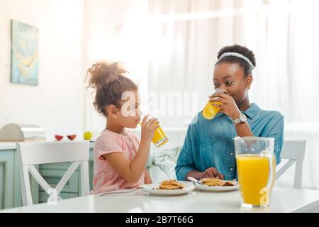 madre e figlia african american bere succo d'arancia vicino a gustosi pancake Foto Stock