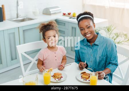 felice madre afro-americana e la figlia guardando la macchina fotografica vicino gustosi pancake Foto Stock