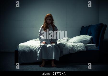 donna ossessionata pazza in una camera da notte seduta a letto Foto Stock