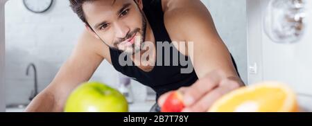 colpo panoramico di bell'uomo che prende fragole dal frigorifero Foto Stock