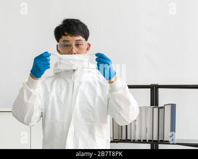 Gli scienziati asiatici ispezionano la qualità di una maschera prima di iniziare l'esperimento in un laboratorio scientifico. Foto Stock