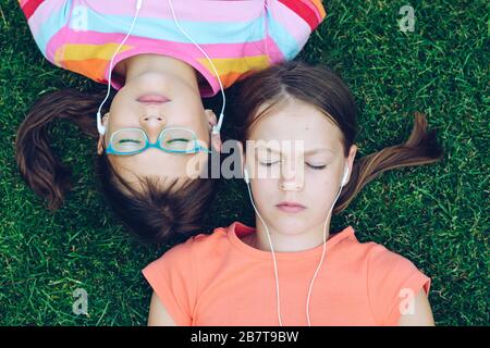 Due ragazze giacciono sull'erba con gli occhi chiusi sulle spalle e ascoltano la musica dalle cuffie Foto Stock