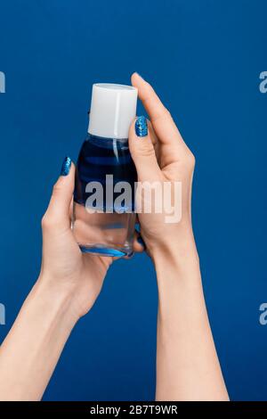 vista tagliata della donna che tiene l'acqua di pulizia micellare isolata su blu Foto Stock