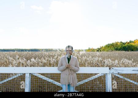 Felice giovane bella donna asiatica che tiene erba contro vista panoramica del campo di bullrush autunno Foto Stock