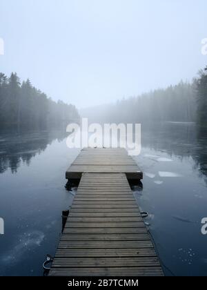 Paesaggio foggy con lago e molo calmi. Nebbia sull'acqua. Aria appannata. Mattina presto freddo in autunno. Bellissimo momento di libertà e atmosfera tranquilla Foto Stock
