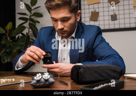 Gioielleria appraiser esame anello gioielli con lente di ingrandimento vicino gioielli e gemme sulla tavola in officina Foto Stock