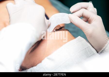 Le mani del cosmetologo si Colle la striscia sotto l'occhio della giovane donna prima della procedura di estensione delle ciglia. Foto Stock