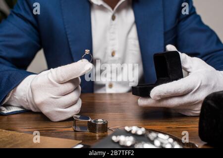 Vista tagliata di gioielli appraiser anello di tenuta con gemstone e scatola sul tavolo su sfondo grigio Foto Stock