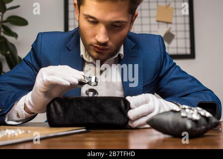 Bei gioielli appraiser tenendo lente d'ingrandimento mentre esaminando gemstone vicino orecchini a tavola Foto Stock