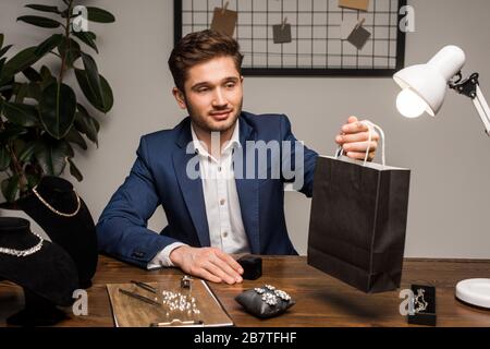 Bel gioiello appraiser che tiene la borsa di carta vicino orecchini e collane sul tavolo Foto Stock