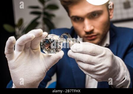 Fuoco selettivo di appraiser di monili nei guanti che esaminano la gemstone con la lente d'ingrandimento nell'officina Foto Stock