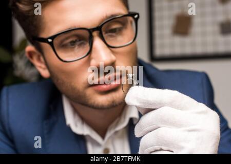 Fuoco selettivo di appraiser di monili in guanto e anello di tenuta degli occhiali con gemstone in officina Foto Stock