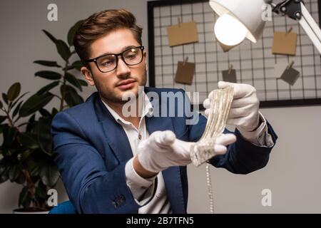 Fuoco selettivo di appraiser della gioielleria che tiene la collana vicino alla lampada in officina Foto Stock