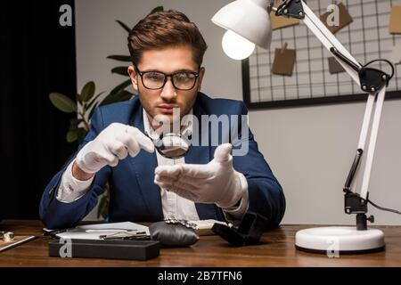 Gioielleria appraiser esame bracciale con lente d'ingrandimento vicino gioielli sulla tavola Foto Stock