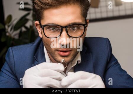 Gioielleria scioccata appraiser in guanti tenuta anello gioielli con gemstone in officina Foto Stock