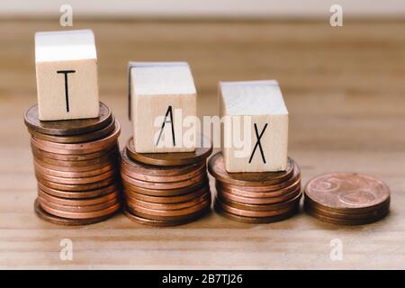 Cubetti di legno con la parola Tax sui soldi che arrampicano i punti di riferimento, mucchio delle monete, fondo di concetto di imposta Foto Stock