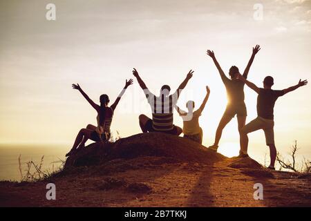 Gruppo di turisti felici si alza e si siede con le braccia sollevate al tramonto e divertirsi Foto Stock