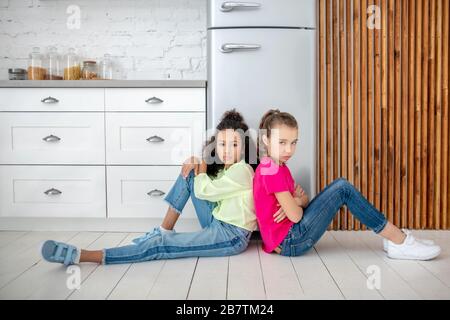 Ragazza dai capelli scuri in jeans seduti accanto al frigo con il suo amico Foto Stock