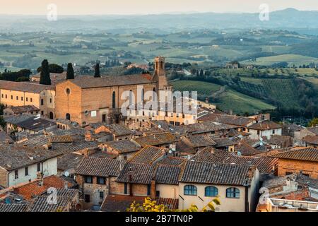 Chiesa di Sant'Agostino e i tetti del centro storico di San Gimignano visti dalla Rocca di Montestaffoli al Parco della Rocca al tramonto. Foto Stock