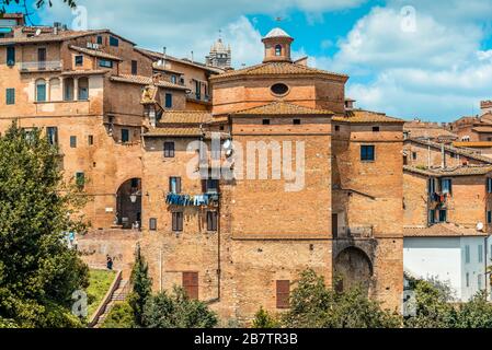 Chiesa di San Giuseppe con la porta Sant'Agata ad arco a sinistra e la cima del campanile del Duomo di Siena sullo sfondo, Siena, Italia Foto Stock