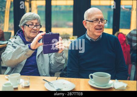 Una donna matura seduta in un bar con suo marito sta utilizzando il suo smartphone per scattare foto Foto Stock