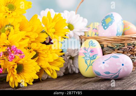 Primo piano di un bouquet di belle margherite gialle e colorate uova di pasqua su una superficie di legno Foto Stock