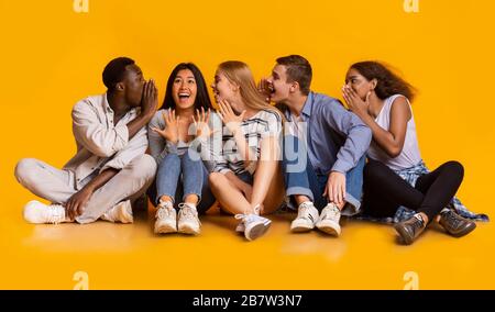 Gruppo di amici multirazziali che condividono gossip su sfondo giallo Foto Stock