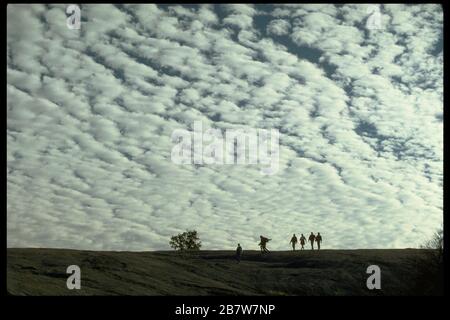 Vicino a Fredericksburg Texas USA: Gli escursionisti dell'Enchanted Rock state Park si trovano in una posizione che si staglia contro il cielo pieno di nuvole di altocumuli. ©Bob Daemmrich Foto Stock