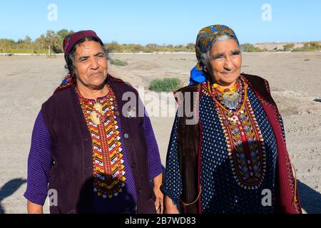 Due donne in posa che indossano abiti tradizionali per l'area rurale in Asia Centrale a Kunya Urgench, Turkmenistan. Colorful Turkmen accappatoio e sciarpa. Foto Stock