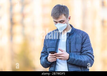 Giovane uomo con maschera protettiva sul suo viso comunica dal telefono cellulare. Concetto di Coronavirus Covid-19. Foto Stock