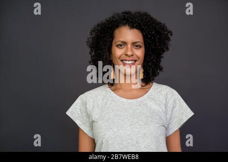 Giovane donna sorridente in piedi su uno sfondo grigio Foto Stock